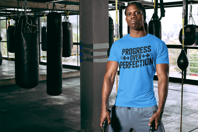 Person wearing a blue t-shirt with 'Progress Over Perfection' text in a gym setting. Progress Over Perfection Tee — Motivational Gym Workout T-Shirt