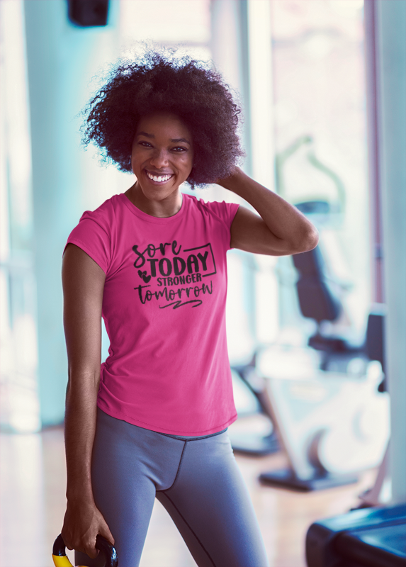 Woman in a gym wearing a pink t-shirt with motivational text Workout T-Shirt — "Sore Today, Stronger Tomorrow" Motivational Gym Tee