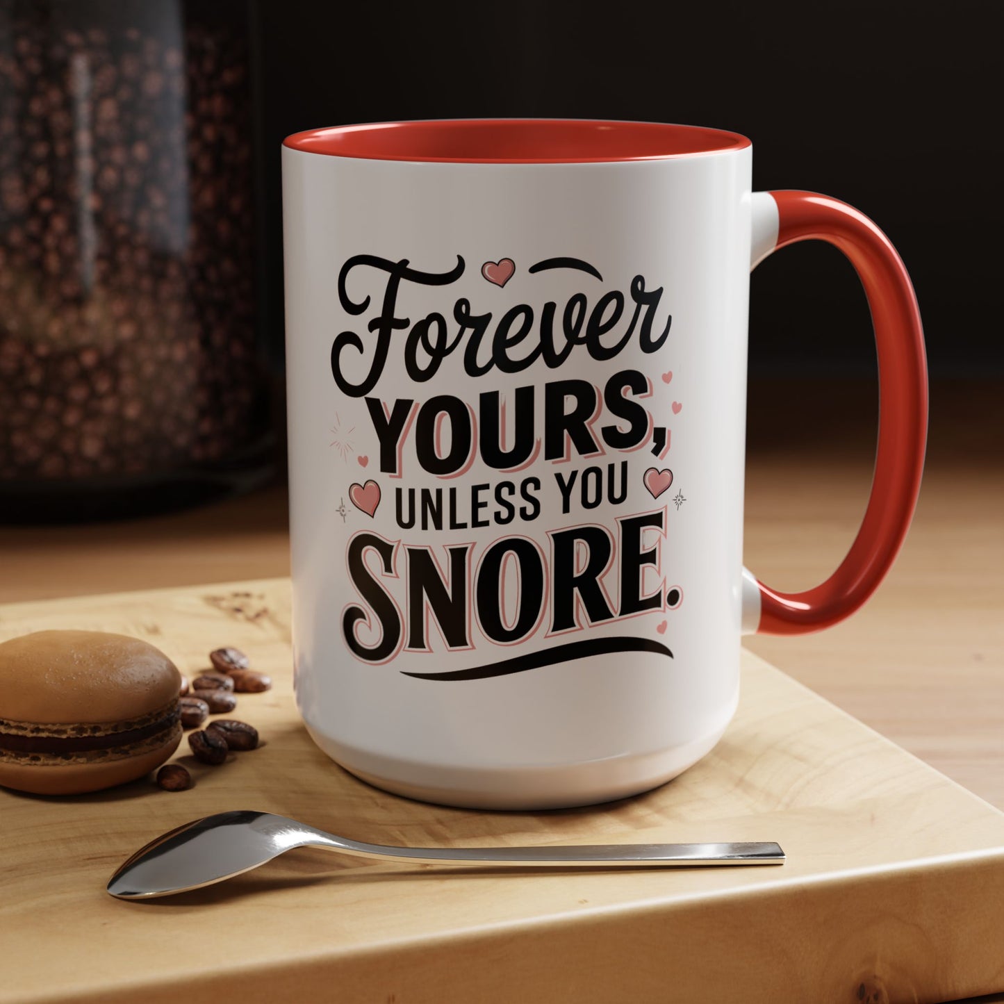 White mug with red interior and handle, featuring a humorous message, on a wooden surface with coffee beans and a spoon.